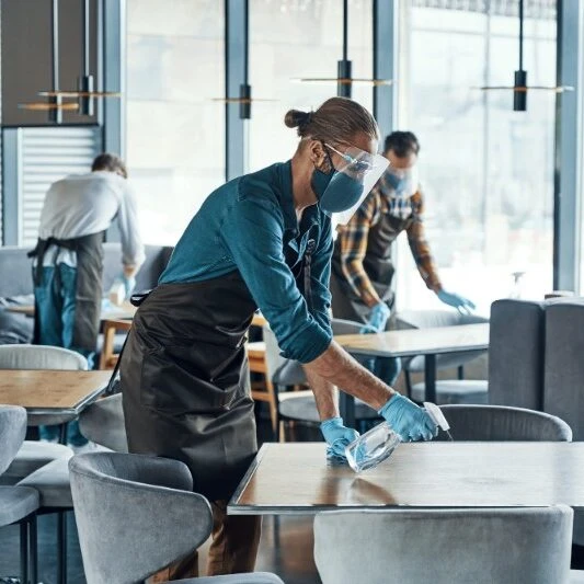 A cleaner is seen tidying a desk while another works in the background. The image showcases professional cleaning in action, with a focus on detail and teamwork.